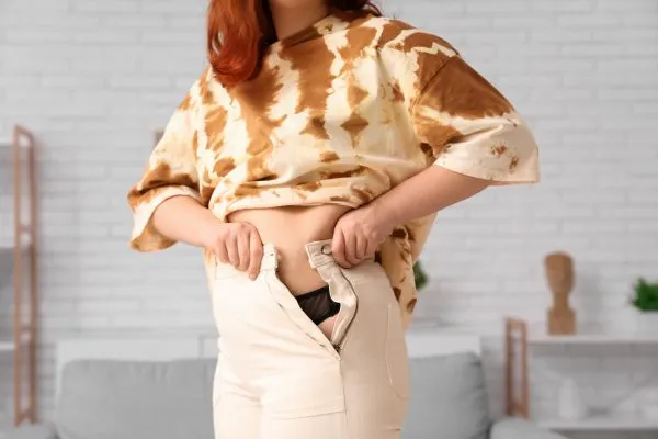 Image of woman trying to do her trousers up after pregnancy weight gain Bicester